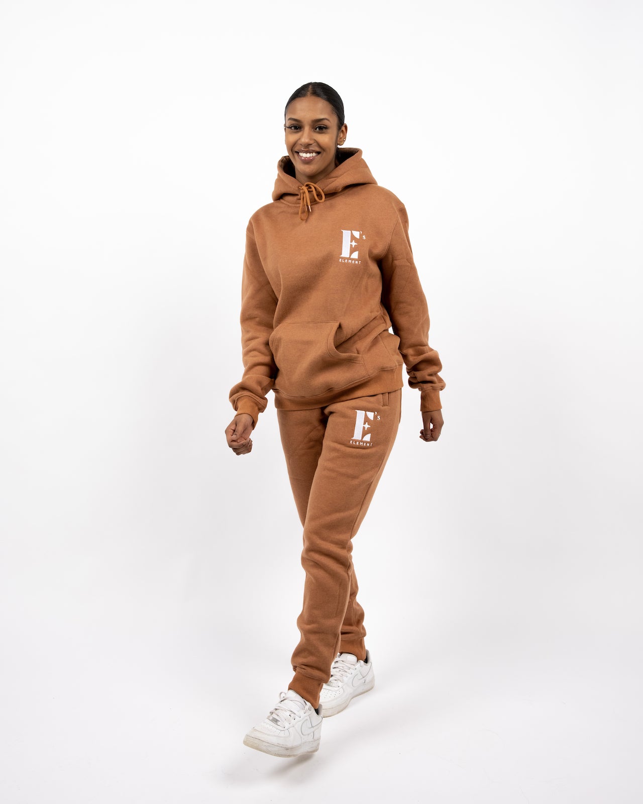Model wearing a light brown sweat suit. The model is also wearing white sneakers. The sweat suit has the E's Element logo imprinted in white. E's Element Essential Brown Sugar Sweatsuit Set by E's Element.