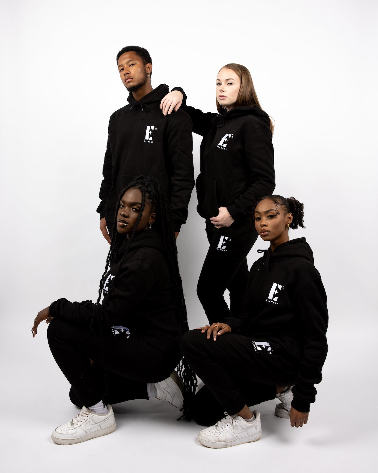 Models wearing black sweatsuits. The sweatsuits are imprinted with the E's Element logo in white. The models are also wearing matching white sneakers.E's Element Essential Smoky Black Sweatsuit Set by E's Element.