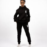Model wearing black track suit. The hoodie and sweat pants has E's Element logo imprinted on it. E's Element Essential Smoky Black Sweatsuit Set by E's Element.