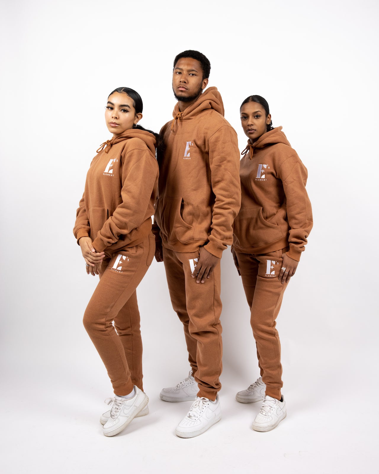 Three models wearing light brown track suits. The tracksuits have the E's Element logo imprinted in white. The models are also wearing white sneakers. E's Element Essential Brown Sugar Sweat suit Set by E's Element.