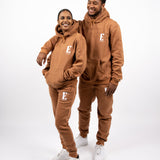 Models wearing matching light brown sweat suits. The sweat suits have the E's Element logo imprinted in white. The models are also wearing matching white sneakers. E's Element Essential Brown Sugar Sweatsuit Set by E's Element.