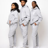 Photos of a male model and two female Model wearing the e's element essential sweatsuit in light grey. in this photo they all show the full outfit with the e's element logo showing on the hoodie and sweatpants.