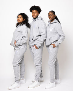 Photos of a male model and two female Model wearing the e's element essential sweatsuit in light grey. in this photo they all show the full outfit with the e's element logo showing on the hoodie and sweatpants.
