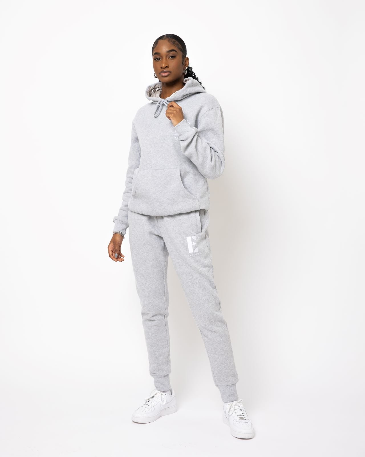 Model posing and wearing a light grey sweat suit. The sweat suit has the E's Element imprinted in white.  Woman wearing grey hoodie and sweatpants.