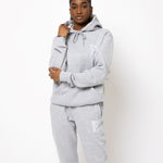 Model posing and wearing a light grey sweat suit. The sweat suit has the E's Element imprinted in white.  Woman wearing grey hoodie and sweatpants.
