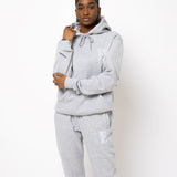 Model posing and wearing a light grey sweat suit. The sweat suit has the E's Element imprinted in white.  Woman wearing grey hoodie and sweatpants.