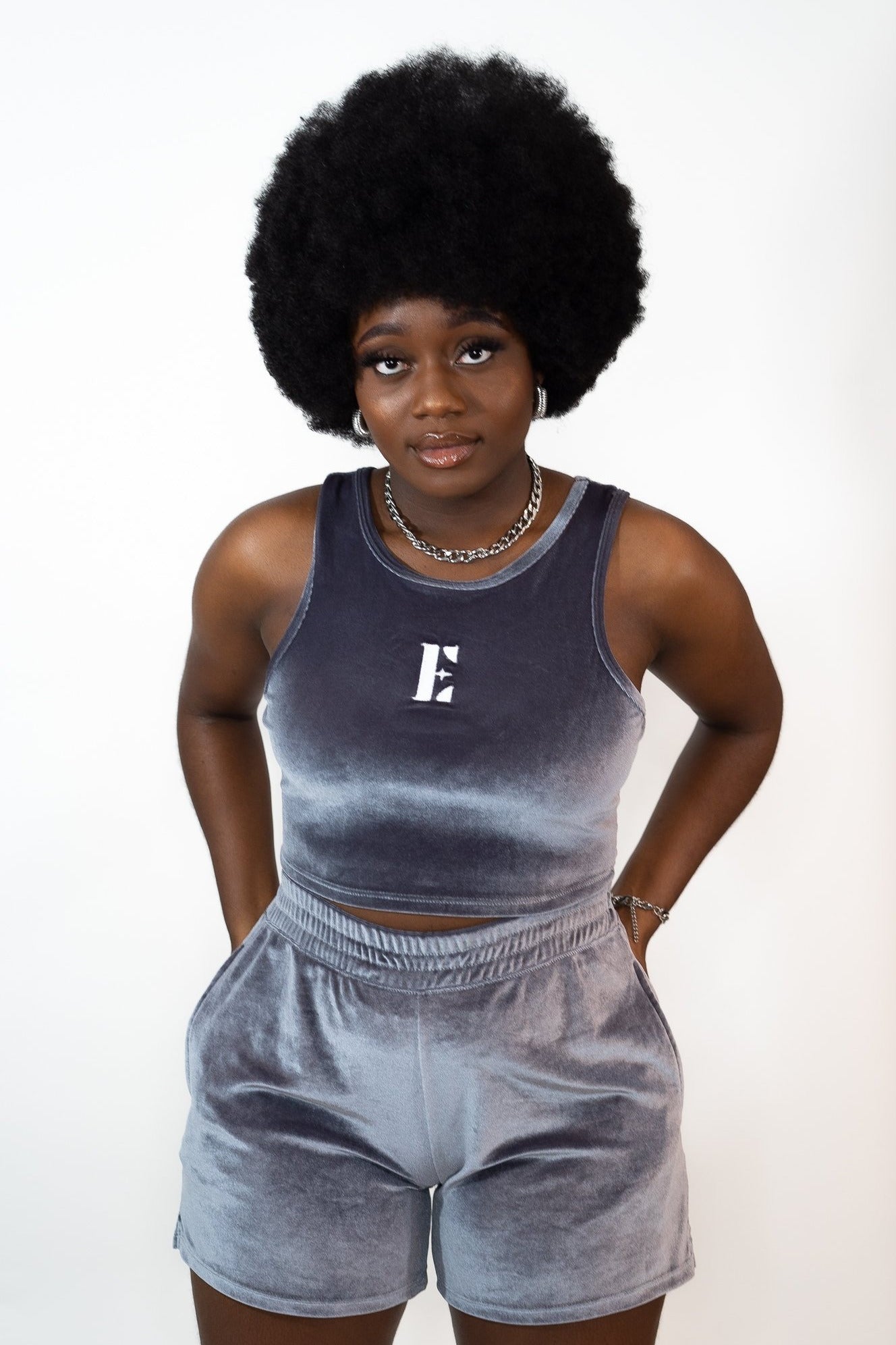 Model wearing grey velvet crop top and shorts. The crop top has the E's Element imprinted in white in the center. The model is also wearing an 18k silver stainless steel chain necklace and hoop earrings. Ella Icy Blue Velvet Set by E's Element.