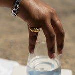 Model holding a glass of water. She is wearing an 18k gold croissant shaped ring. She is also wearing a silver chain bracelet. Thick Croissant Rings by E's Element.