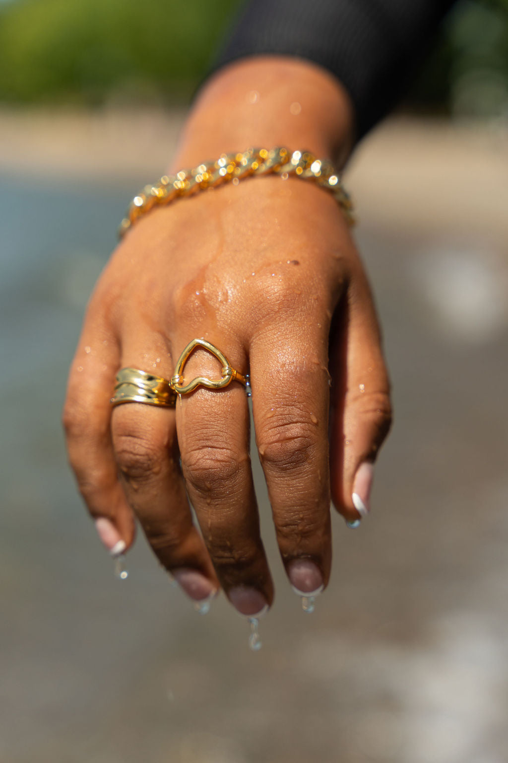 Model in a black top wearing 18k gold heart shaped ring. The model is also wearing another 18k gold ring on the ring finger and a chain bracelet. Ella's Element Hollow Heart Out Ring by E's Element.