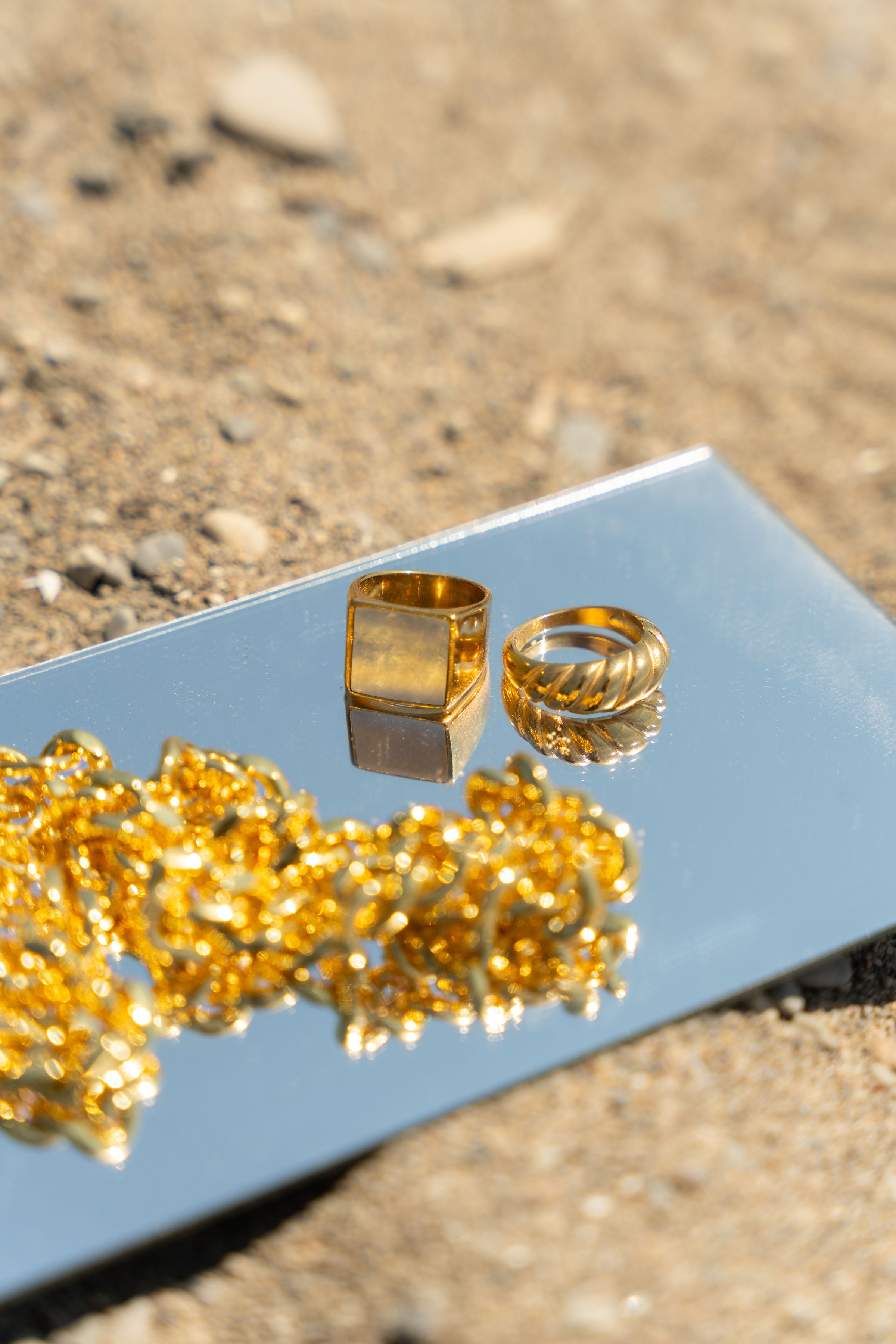 Two 18k gold stainless steel rings and a necklace resting on top of a mirror. Build Your Own Jewelry Set by E's Element.