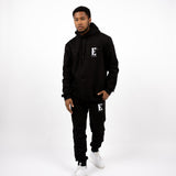 Model wearing a black sweat suit. The hoodie and sweat pants has the E's Element logo imprinted in white. The model is also wearing white sneakers. E's Element Essential Smoky Black Sweatsuit Set by E's Element.