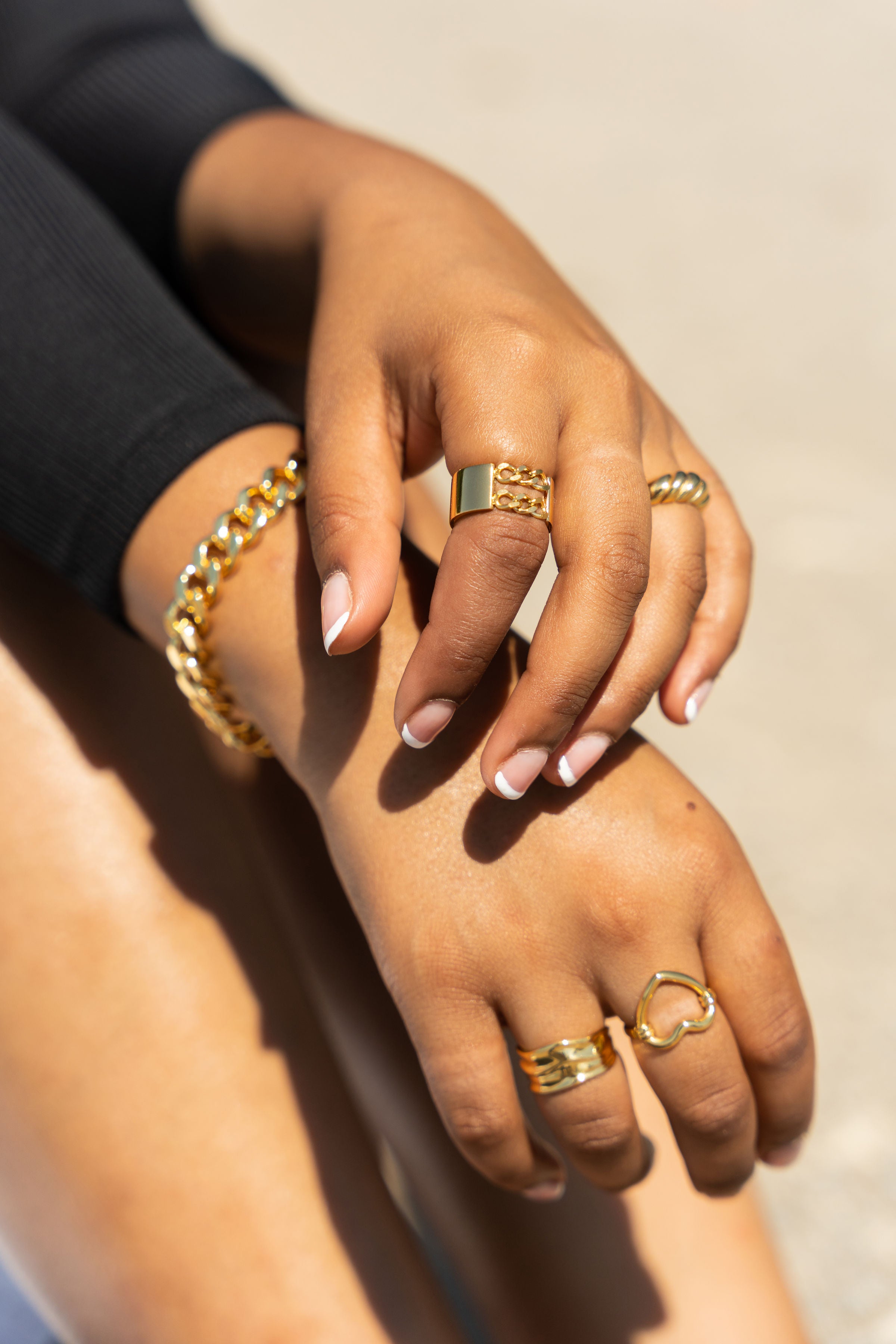 Woman in black top wearing 18k gold stainless steel jewelry set. The gold jewelry set she is wearing consists of a bracelet and rings on both hands. Build Your Own Gold Jewelry Set by E's Element.