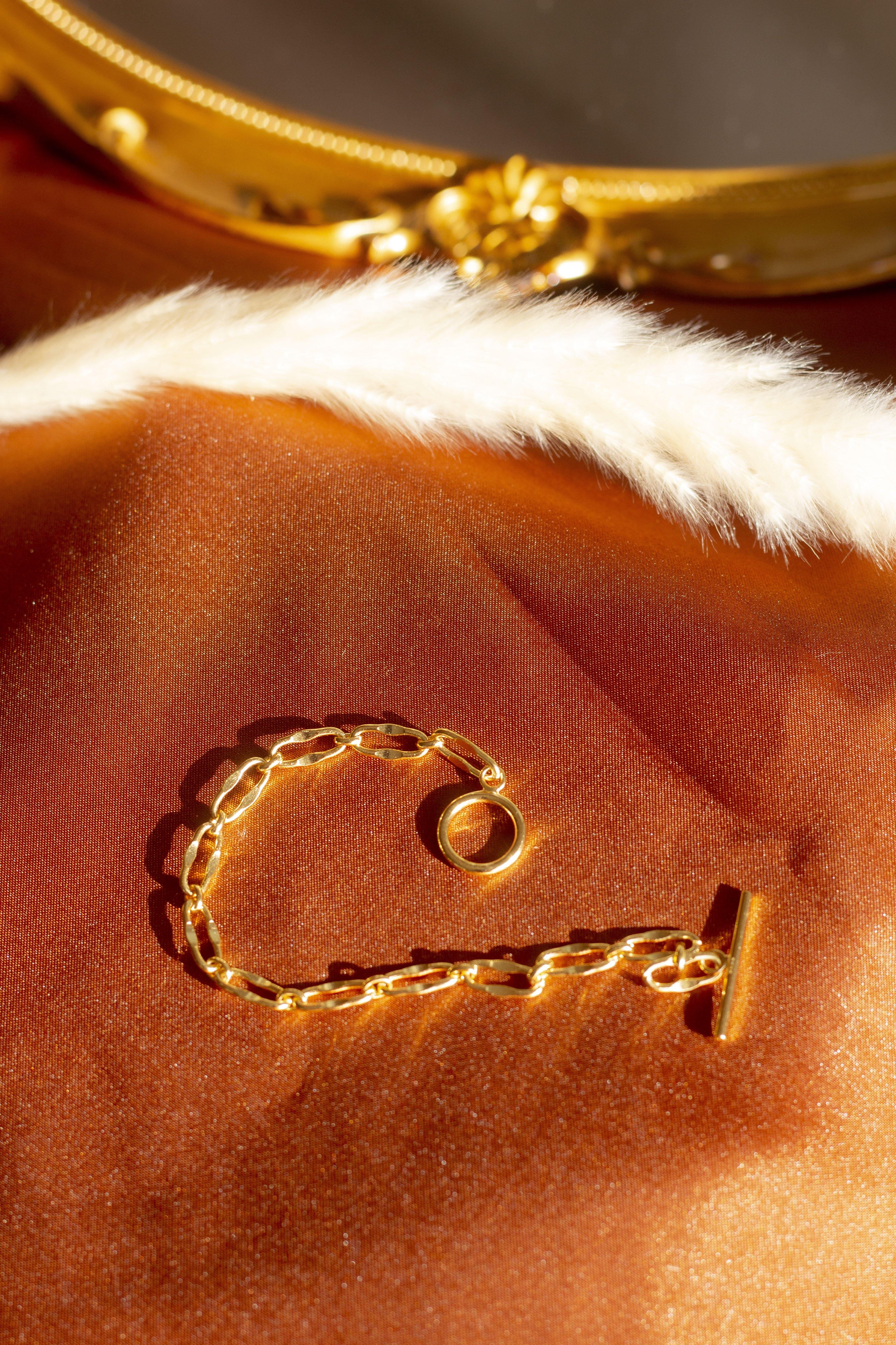 18k gold chain bracelet resting on an orange cloth. The bracelet has a hollow circle charm. Hollow Signature Chain Bracelet by E's Element by Emmanuela Okon.