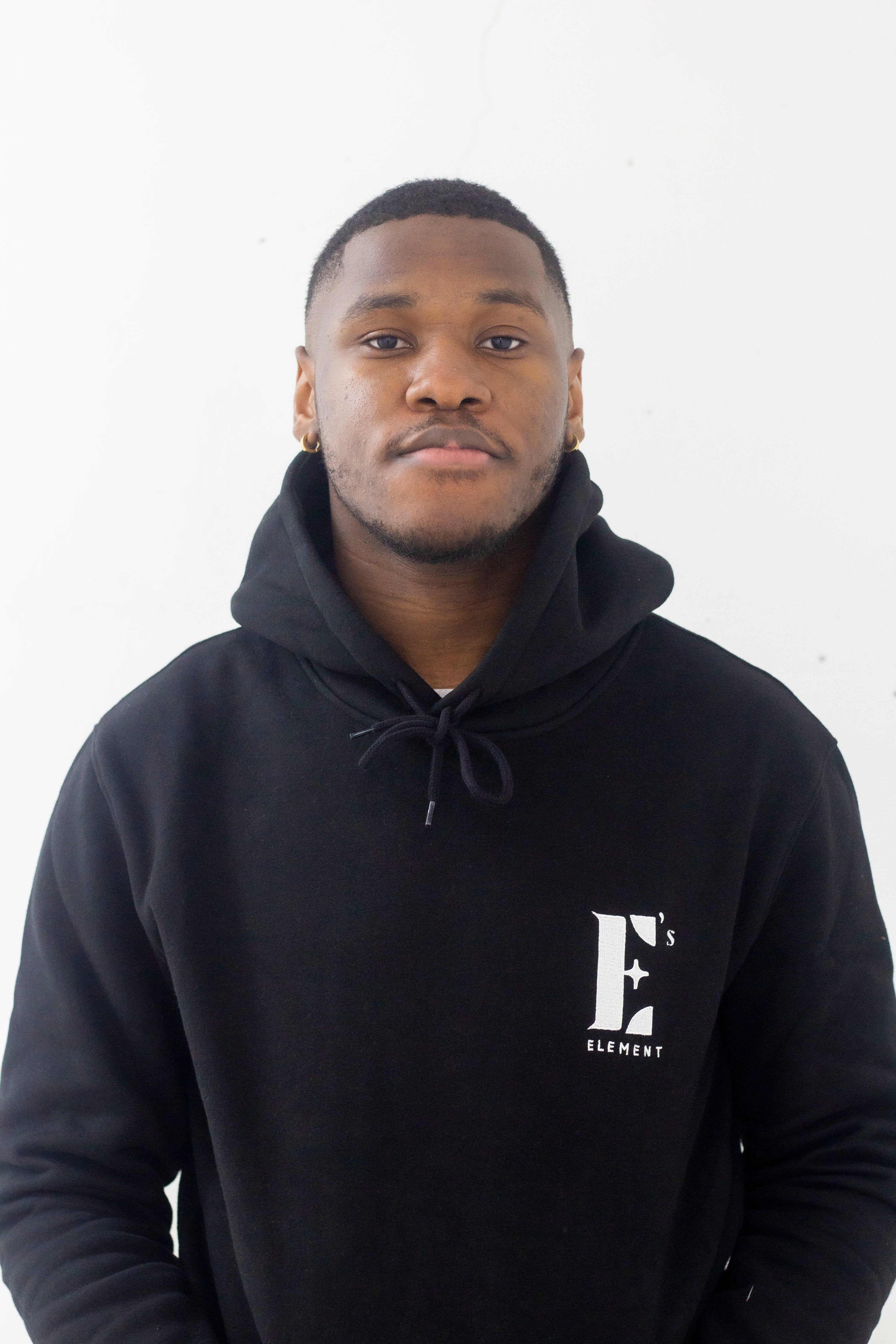 Model wearing a black hoodie. The hoodie has the E's Element logo imprinted in white. E's Element Essential Smoky Black Sweatsuit Set by E's Element.