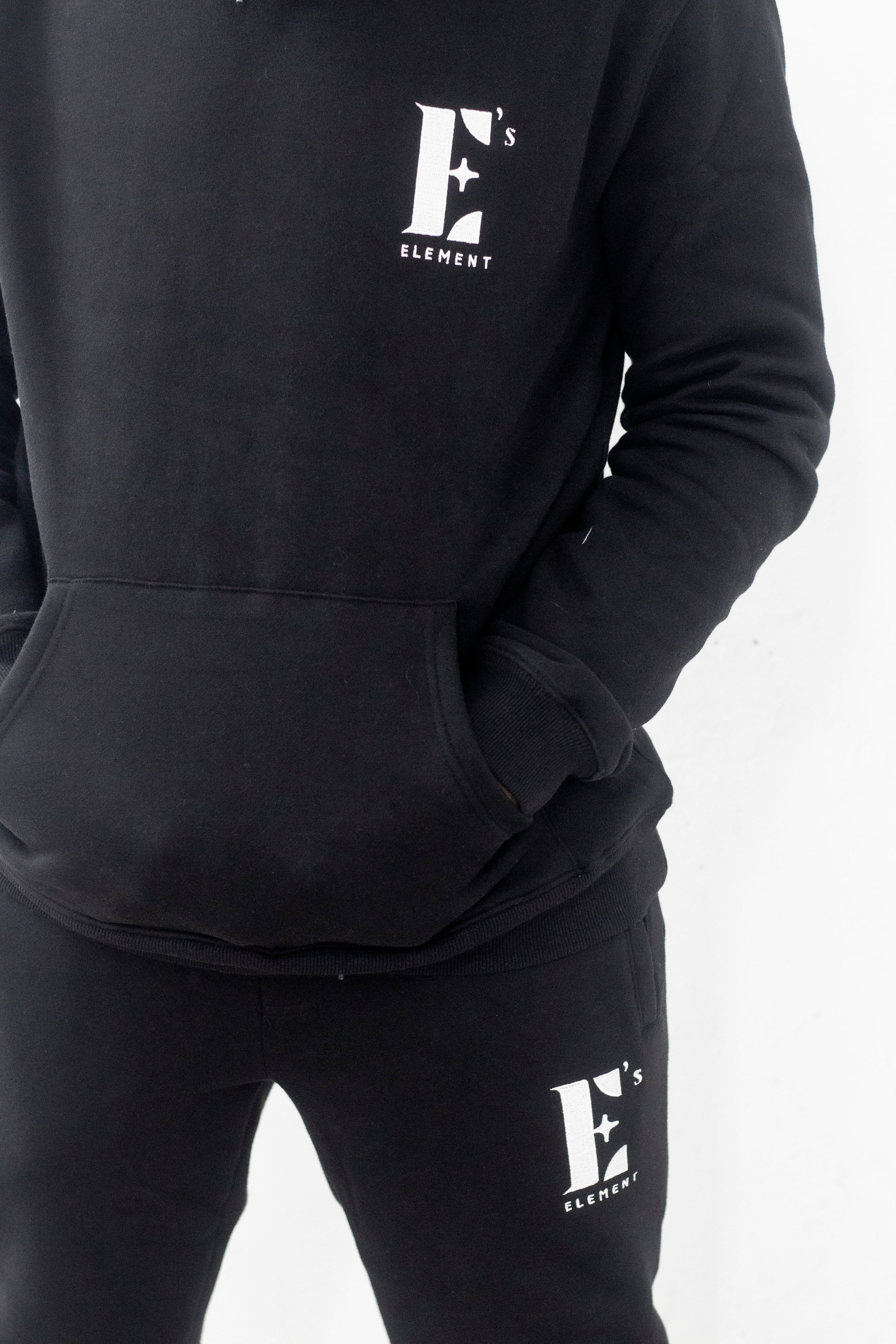 Model wearing a black sweat suit. The hoodie and sweat pants have the E's Element logo imprinted in white. E's Element Essential Smoky Black Sweatsuit Set by E's Element.