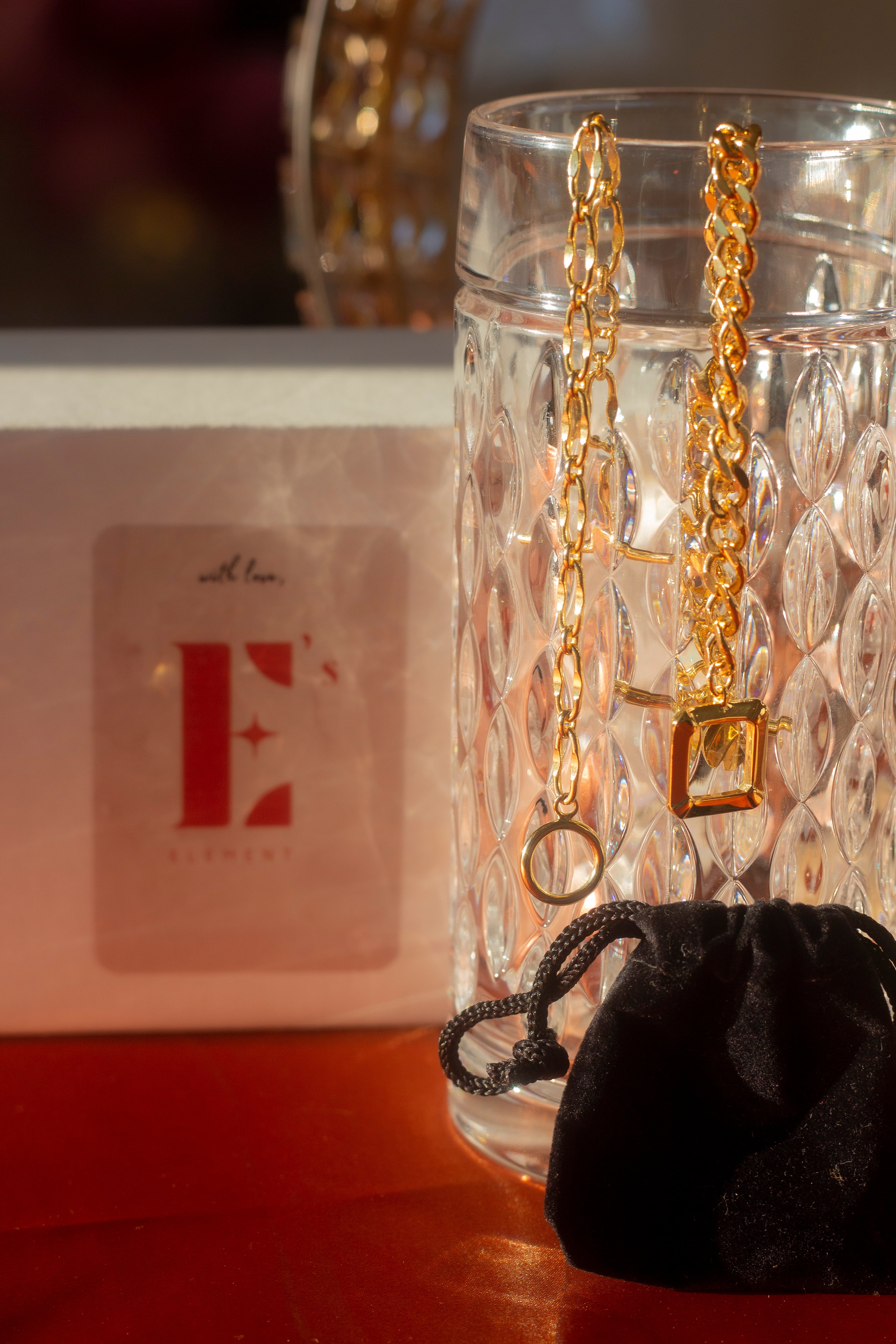 18k gold chain bracelet hanging on the edge of a class cup. Ella Chunky Charm Bracelet by E's Element.