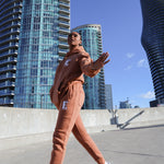 Model wearing a light brown sweat suit. The model is also wearing white sneakers. The sweat suit has the E's Element logo imprinted in white. E's Element Essential Brown Sugar Sweatsuit Set by E's Element.