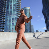 Model wearing a light brown sweat suit. The model is also wearing white sneakers. The sweat suit has the E's Element logo imprinted in white. E's Element Essential Brown Sugar Sweatsuit Set by E's Element.
