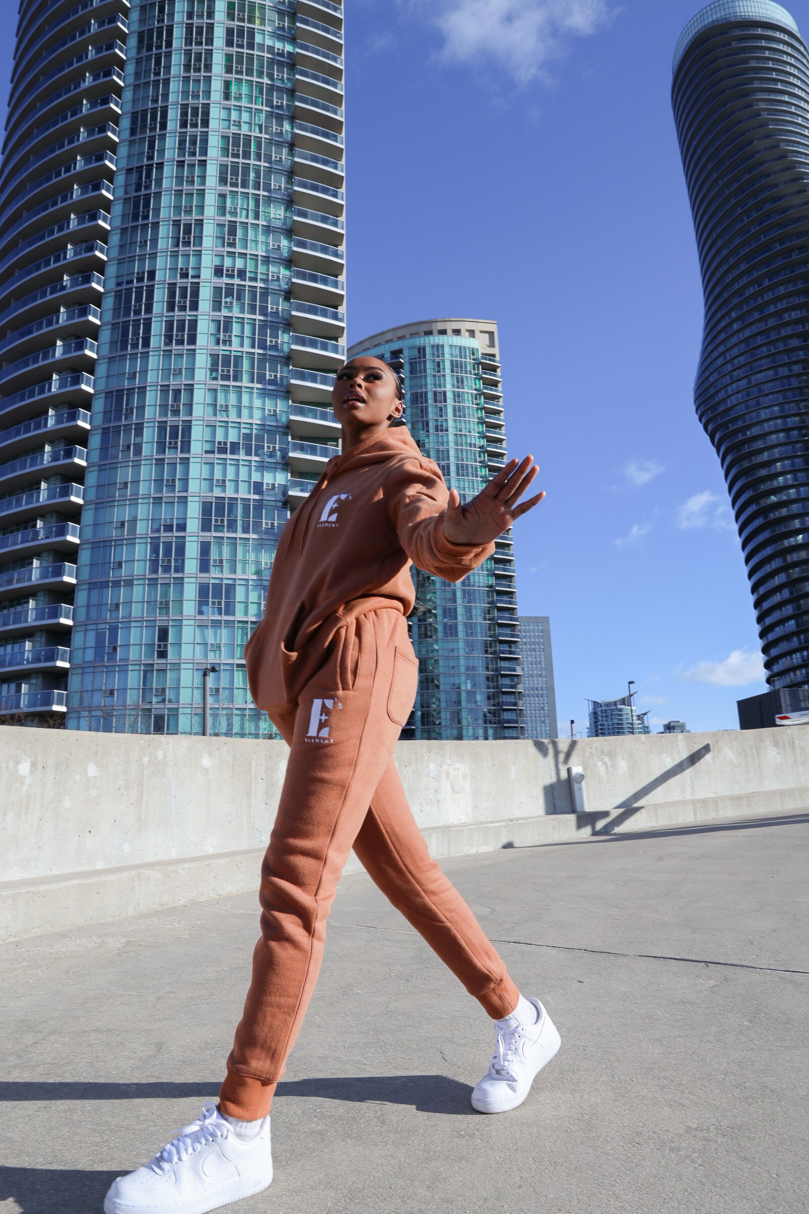 Model wearing a light brown sweat suit. The model is also wearing white sneakers. The sweat suit has the E's Element logo imprinted in white. E's Element Essential Brown Sugar Sweatsuit Set by E's Element.