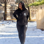 Model wearing a black sweat suit walking in the snow. The hoodie and sweat pants has the E's Element logo imprinted in white. E's Element Essential Smoky Black Sweatsuit Set by E's Element.