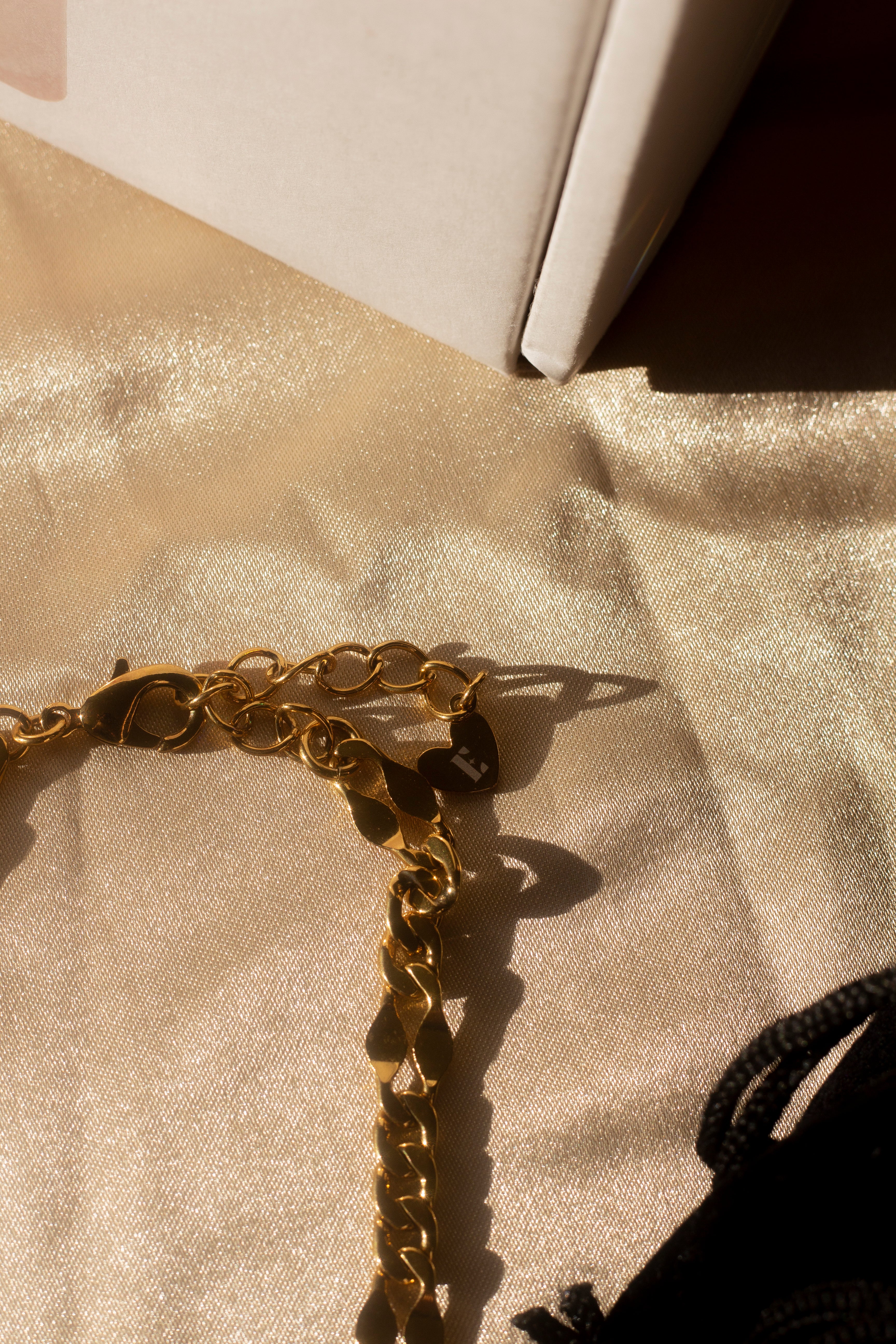 18k gold chain necklace placed on a beige cloth. Above the necklace is a white box. Ella Figaro Necklace by E's Element.