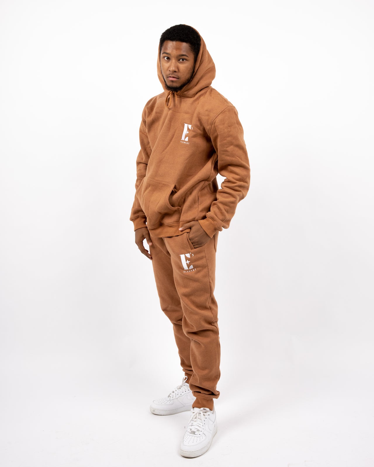 Model wearing a light brown sweat suit. The model is also wearing white sneakers. The sweat suit has the E's Element logo imprinted in white. E's Element Essential Brown Sugar Sweatsuit Set by E's Element.
