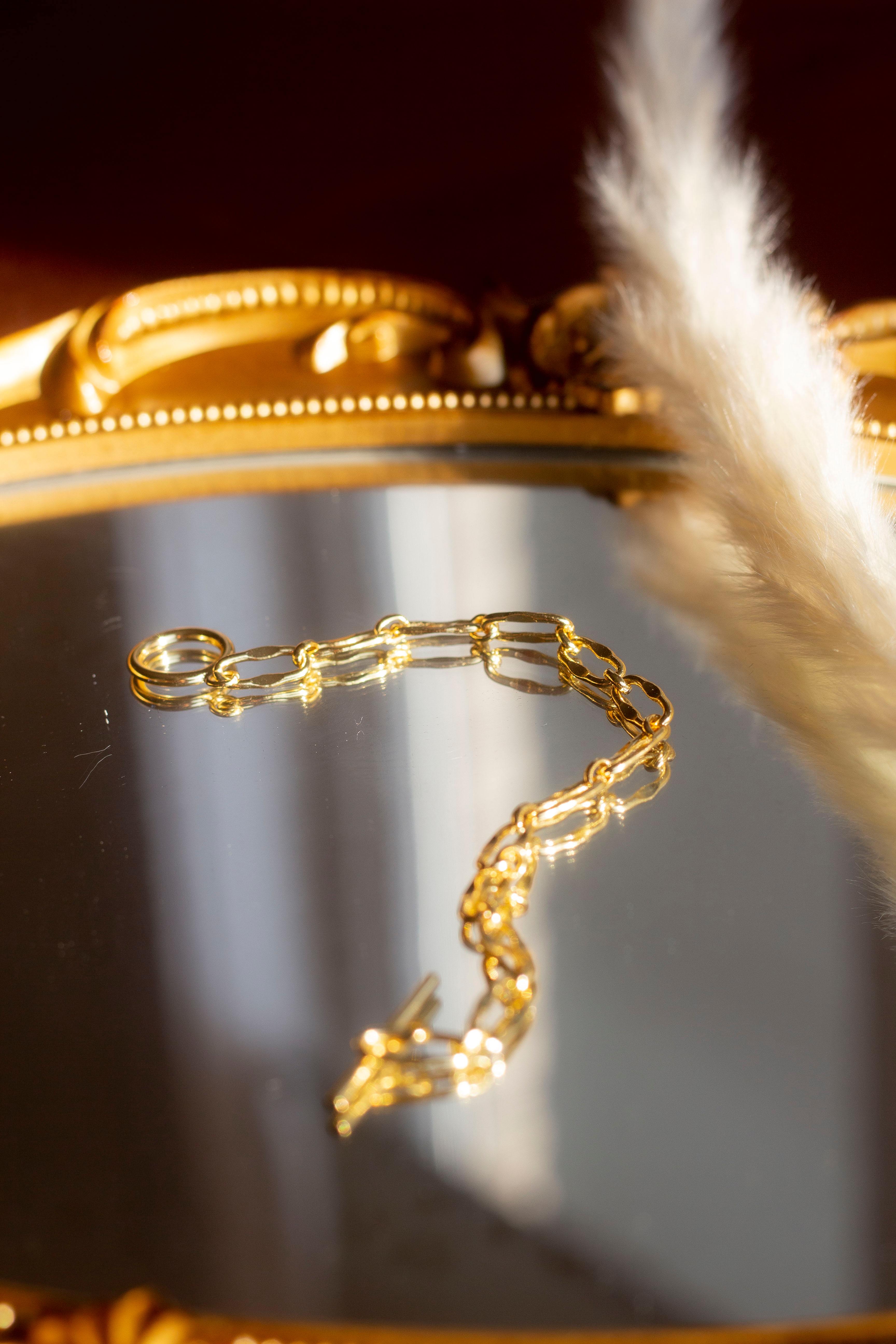 18k gold chain bracelet resting on a mirror with gold edges. The bracelet has a round hollow charm. Hollow Signature Chain Bracelet by E's Element by Emmanuela Okon.