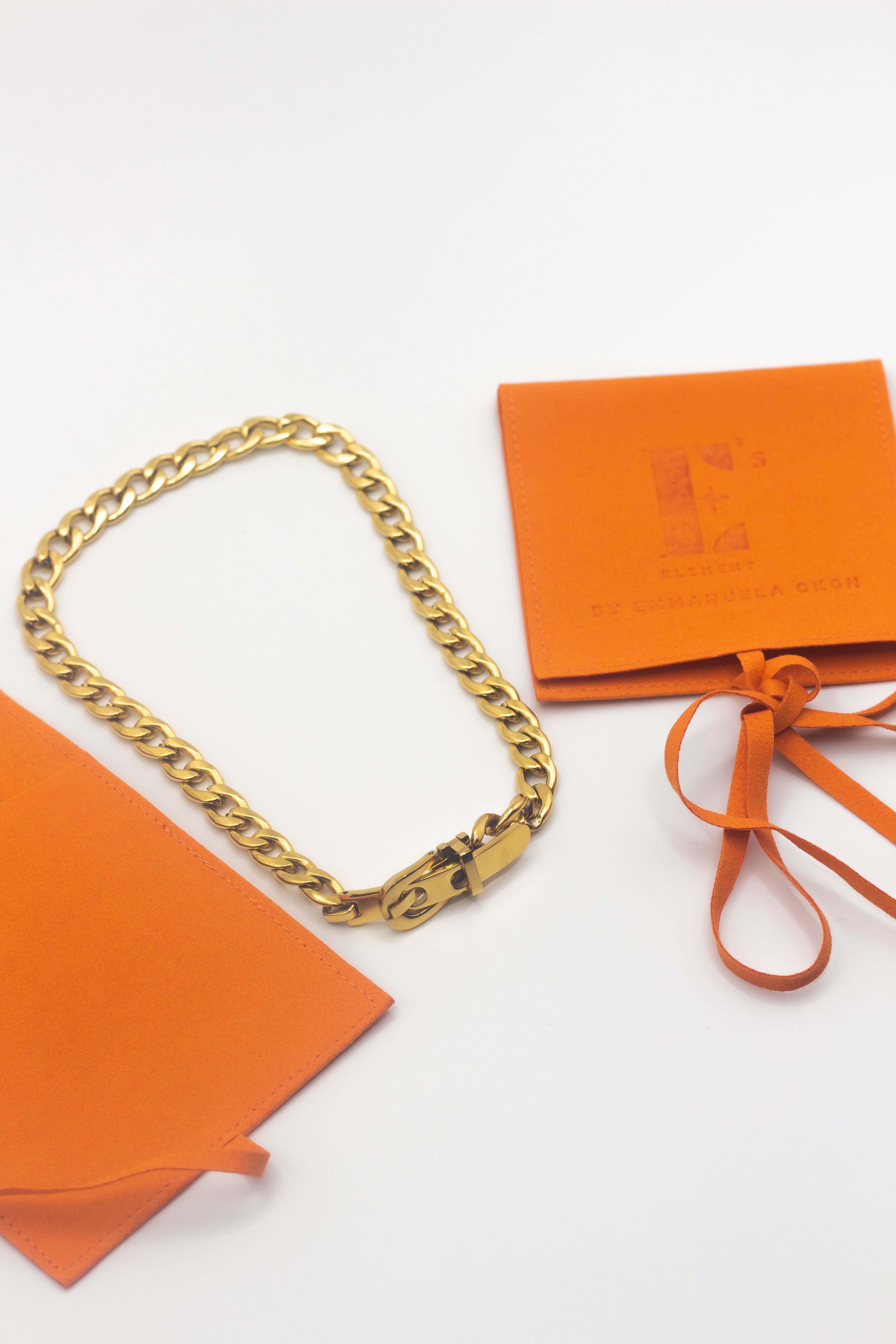 18k gold stainless steel buck chain choker placed in between two orange leather packaging. Ella Buckle Choker by E's Element.
