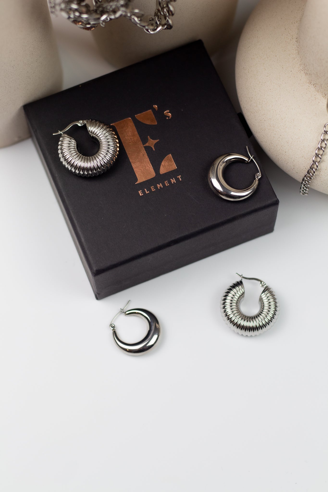 Two pairs of stainless steel earrings resting on their container. Build Your Own Earring Set by E's Element.