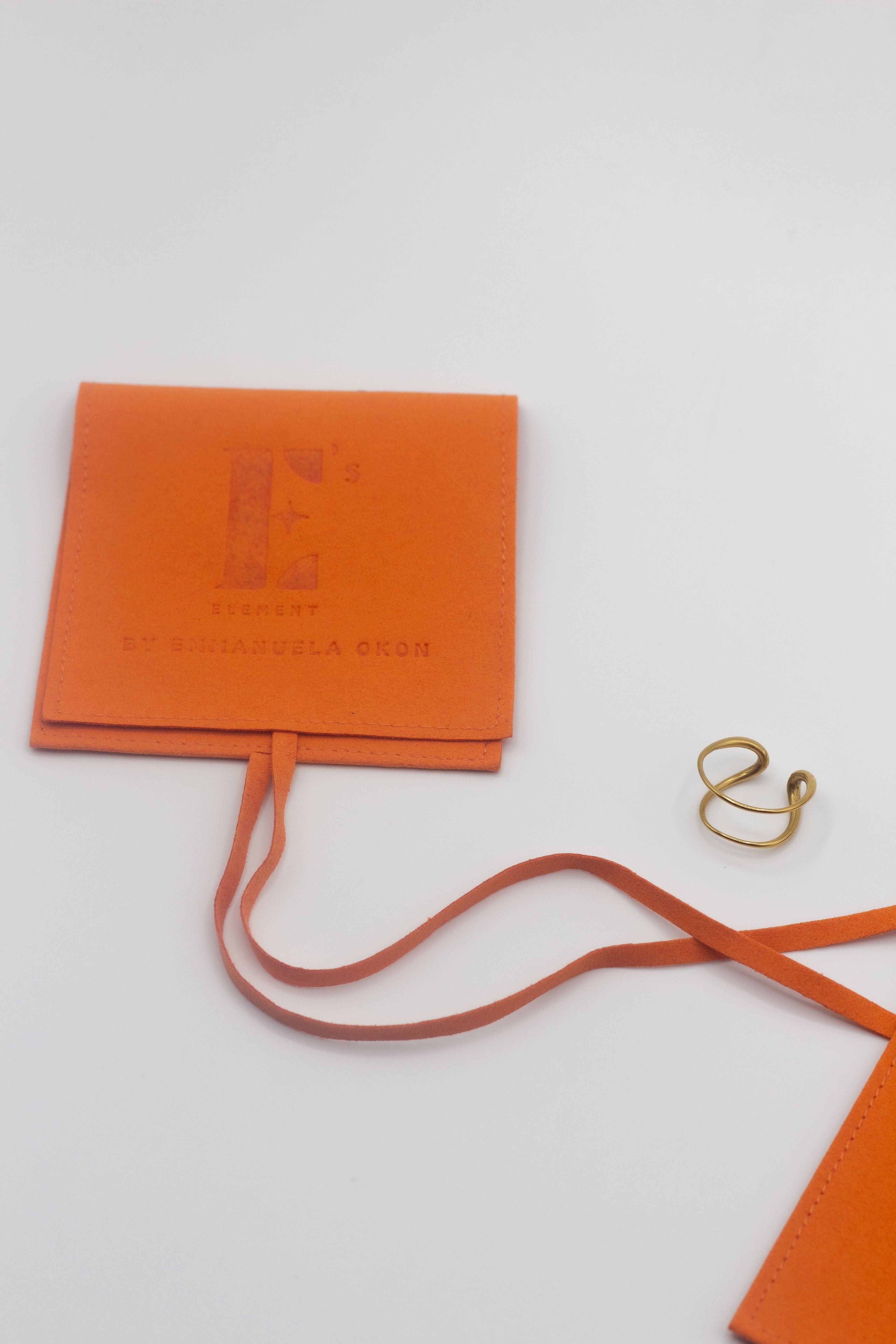18k gold spiral ear cuff on the right. On the left is an orange leather pouch with the E's Element Logo engraved. Unisex Spiral Ear Cuffs - E's Element.