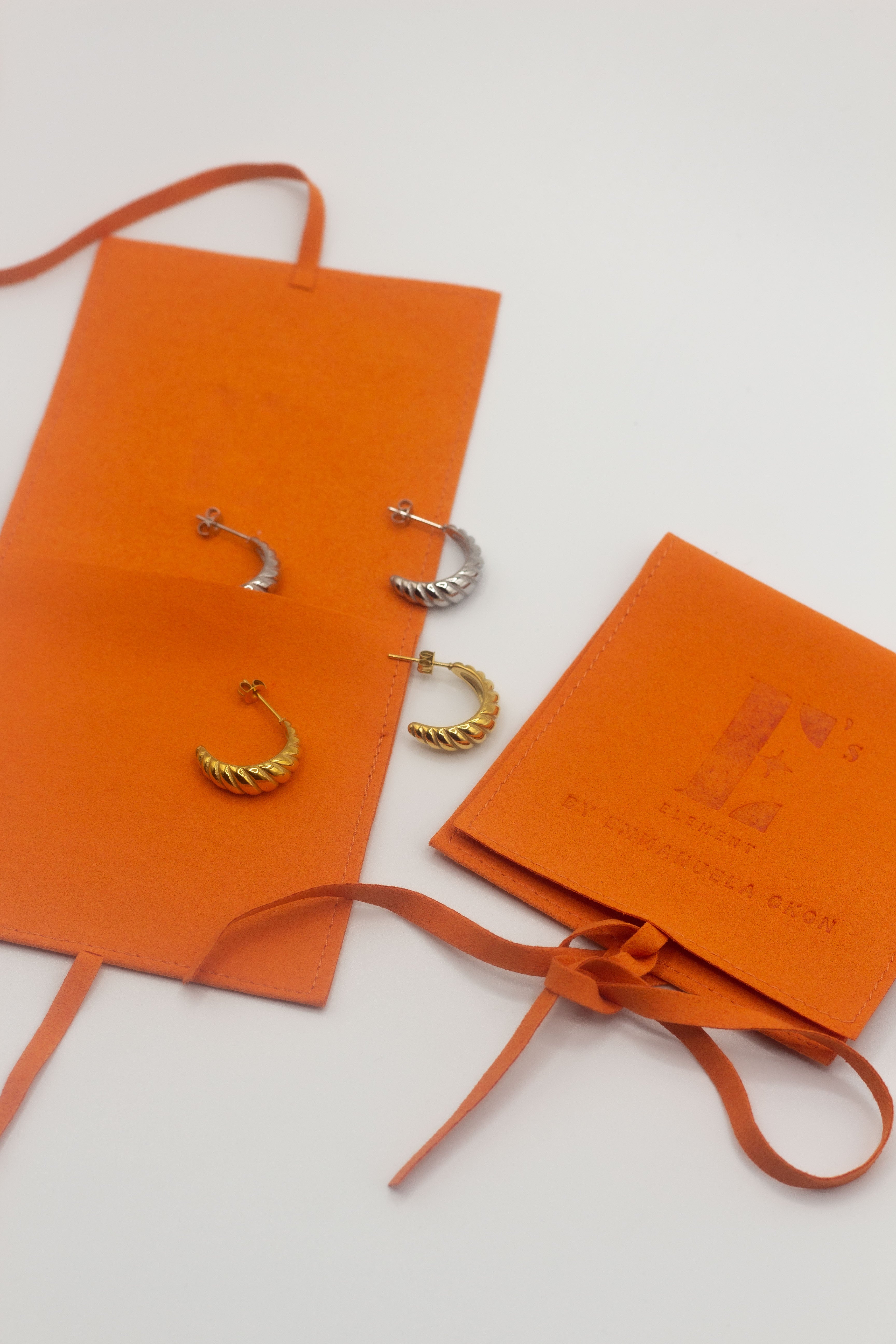 18k gold croissant shaped earrings placed in orange leather pouches. Thick Croissant Stud Earrings - E's Element.