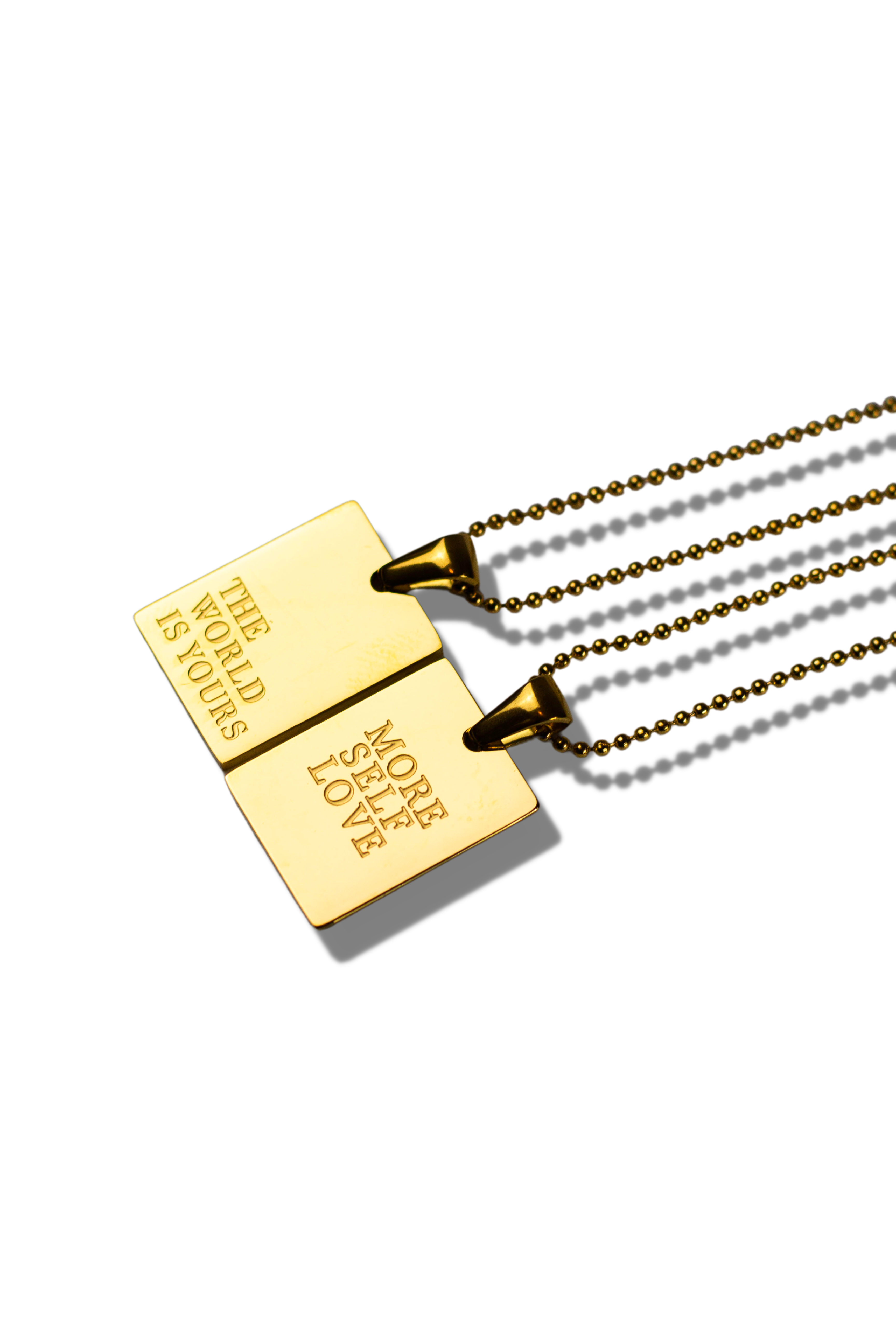 Two 18K stainless steel gold necklaces. The words printed on one of the necklaces are, "THE WORLD IS YOURS" and "MORE SELF LOVE" on the other necklace. The picture is presented sideways.