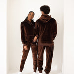 Photo of a male and female model posing in the e's element chocolate brown velvet jogger set. the female model is is showing the front view of the jogger set while the male model is showing the back view of the jogger set.