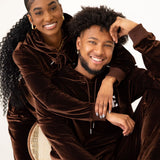 Up close photos of a female and male model wearing the e's element chocolate brown velvet jogger set. This picture shows the details on the hoodie such as the adjustable hood strings, wrist  and ankle details and the e's element logo places on the right hand side of the picture.