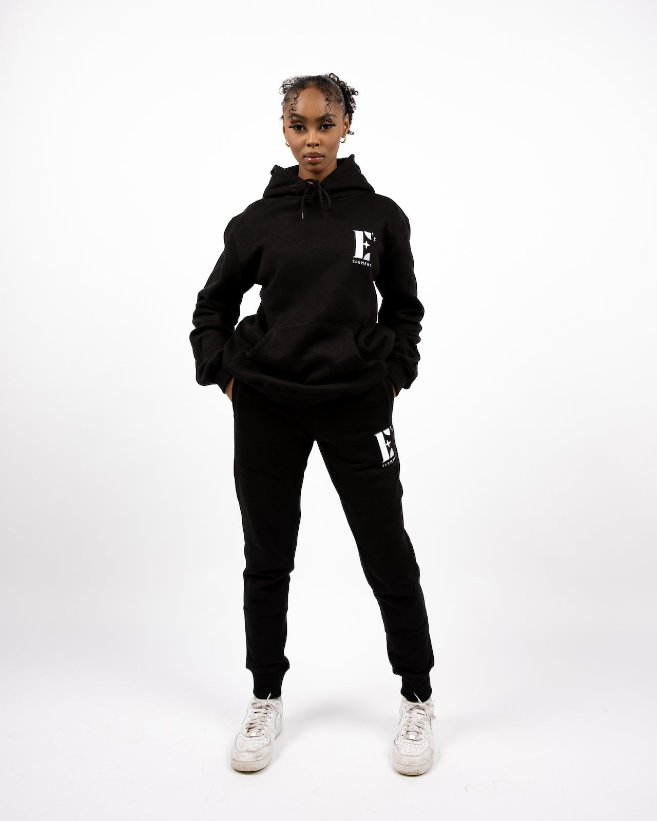 Model wearing black track suit. The hoodie and sweat pants has E's Element logo imprinted on it. E's Element Essential Smoky Black Sweatsuit Set by E's Element.