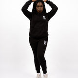 Model wearing a black track suit. The hoodie and sweat pants has the E's Element logo imprinted in white. E's Element Essential Smoky Black Sweatsuit Set by E's Element.