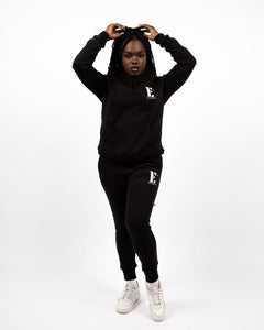 Model wearing a black track suit. The hoodie and sweat pants has the E's Element logo imprinted in white. E's Element Essential Smoky Black Sweatsuit Set by E's Element.