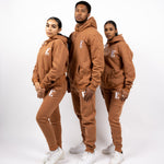 Three models wearing light brown track suits. The tracksuits have the E's Element logo imprinted in white. The models are also wearing white sneakers. E's Element Essential Brown Sugar Sweat suit Set by E's Element.