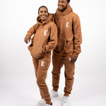 Models wearing matching light brown sweat suits. The sweat suits have the E's Element logo imprinted in white. The models are also wearing matching white sneakers. E's Element Essential Brown Sugar Sweatsuit Set by E's Element.