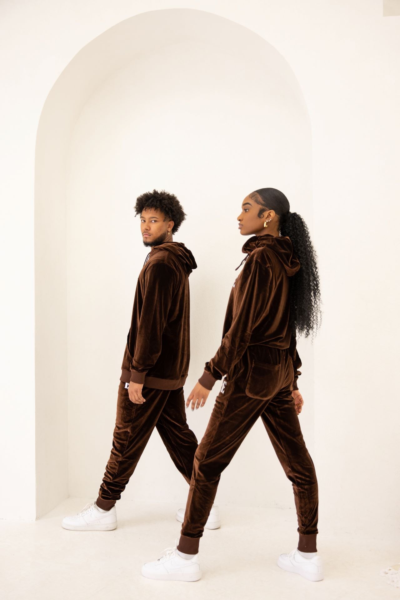 Photo of a male and female model posing in the e's element chocolate brown velvet jogger set. the male and female model is showing the side view of the jogger set.