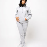 Model posing and wearing a light grey sweat suit. The sweat suit has the E's Element imprinted in white.  Woman wearing grey hoodie and sweatpants.