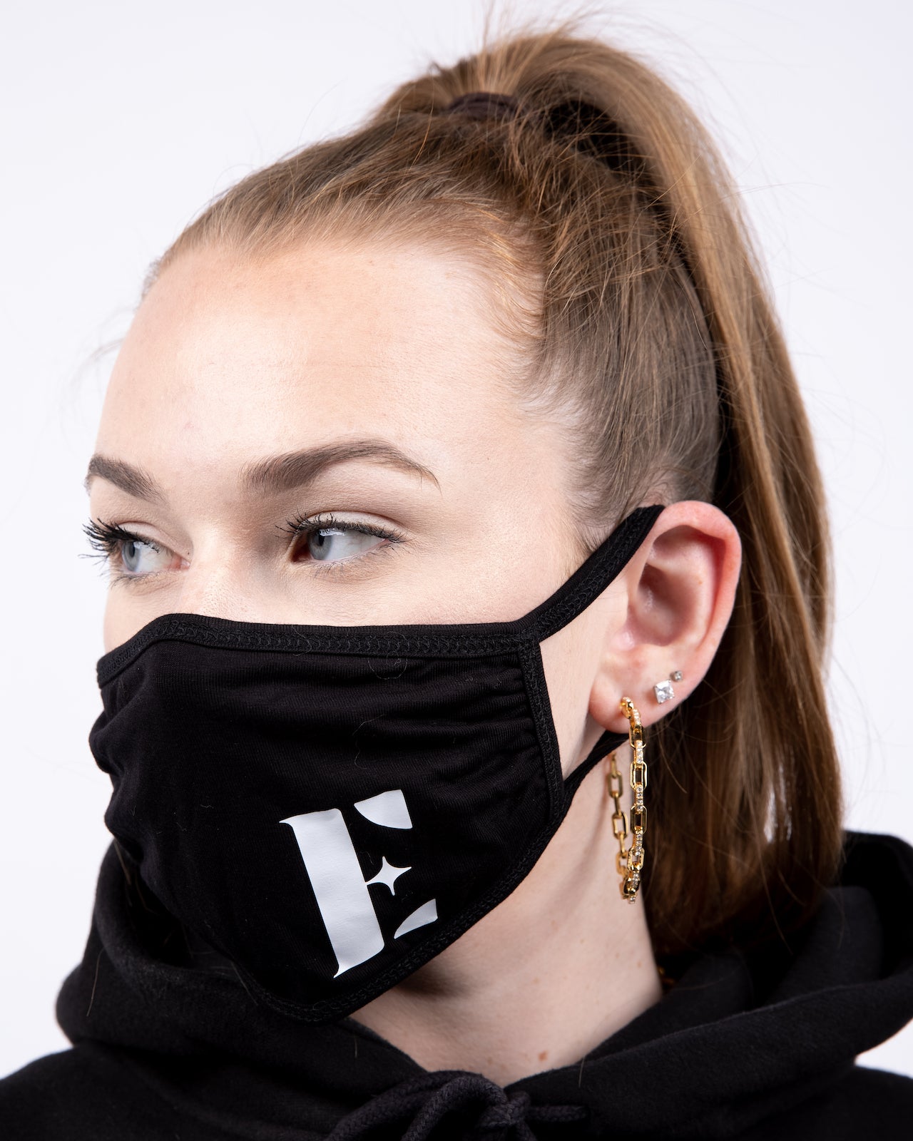 Model in a black hoodie wearing a black reusable face mask. The face mask has the E's Element logo imprinted in white. Smoky Black Face Mask by E's Element.