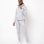 Model posing and wearing a light grey sweat suit. The sweat suit has the E's Element imprinted in white.  Woman wearing grey hoodie and sweatpants.