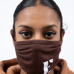 Woman in a light brown hoodie wearing E's Element reusable face mask. The face mask is imprinted with the E's Element logo in white on the bottom left. Chocolate Face Mask by E's Element.
