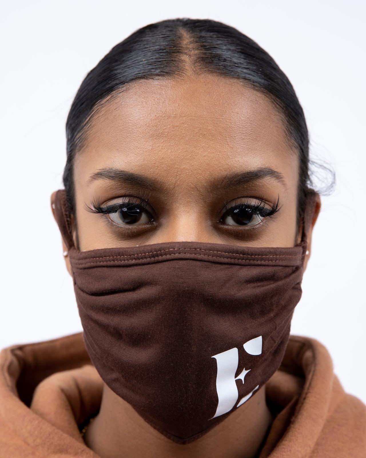 Woman in a light brown hoodie wearing E's Element reusable face mask. The face mask is imprinted with the E's Element logo in white on the bottom left. Chocolate Face Mask by E's Element.