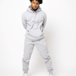 Model posing and wearing a light grey sweat suit. The sweat suit has the E's Element imprinted in white.  Man wearing grey hoodie and sweatpants.