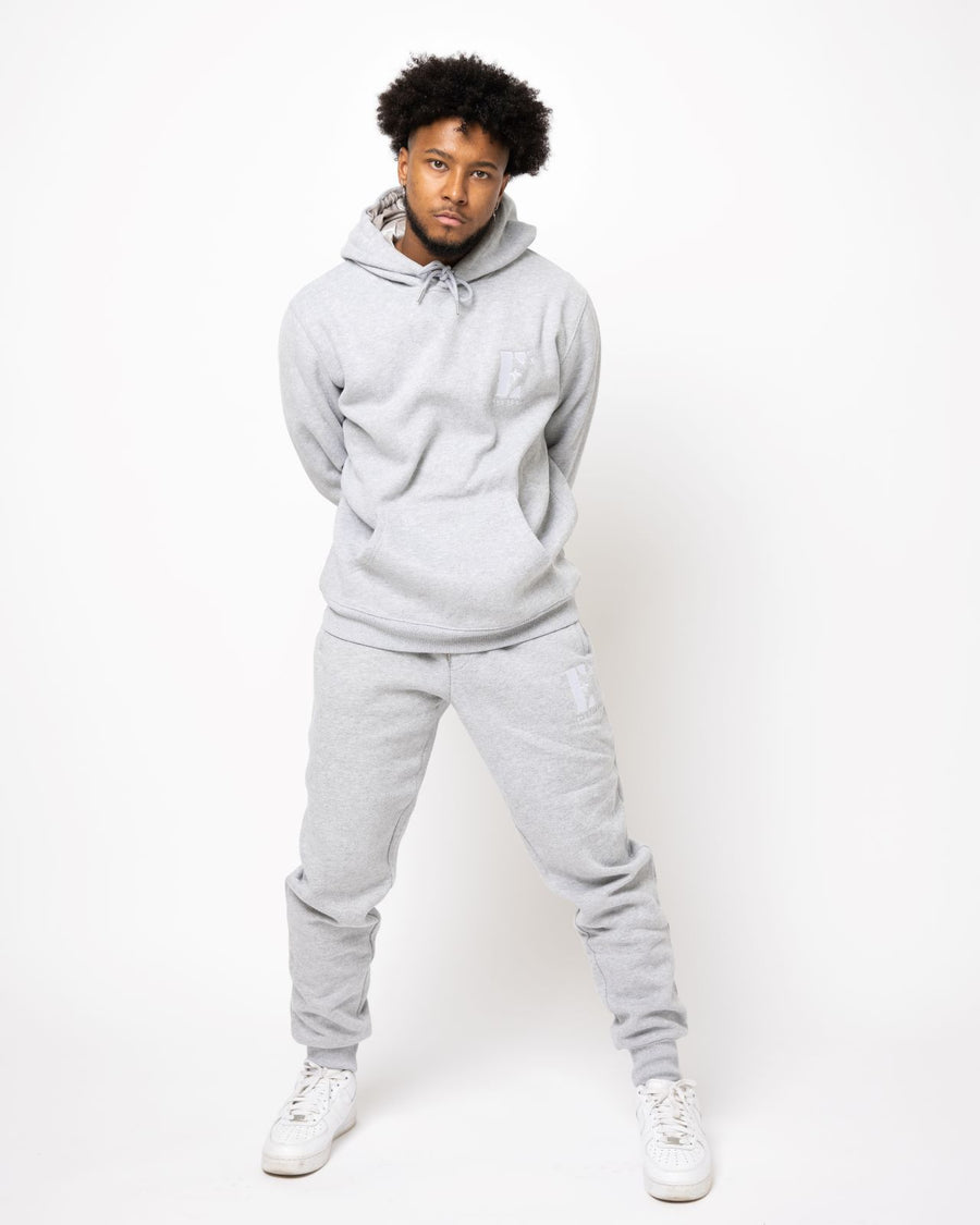 Model posing and wearing a light grey sweat suit. The sweat suit has the E's Element imprinted in white.  Man wearing grey hoodie and sweatpants.