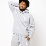 Model posing and wearing a light grey sweat suit. The sweat suit has the E's Element imprinted in white. Man wearing grey hoodie and sweatpants.