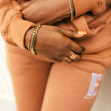 Woman wearing an orange track suit. She is wearing 18k gold stainless steel chain anklet on both wrists. Cuban Link Anklet by E's Element.