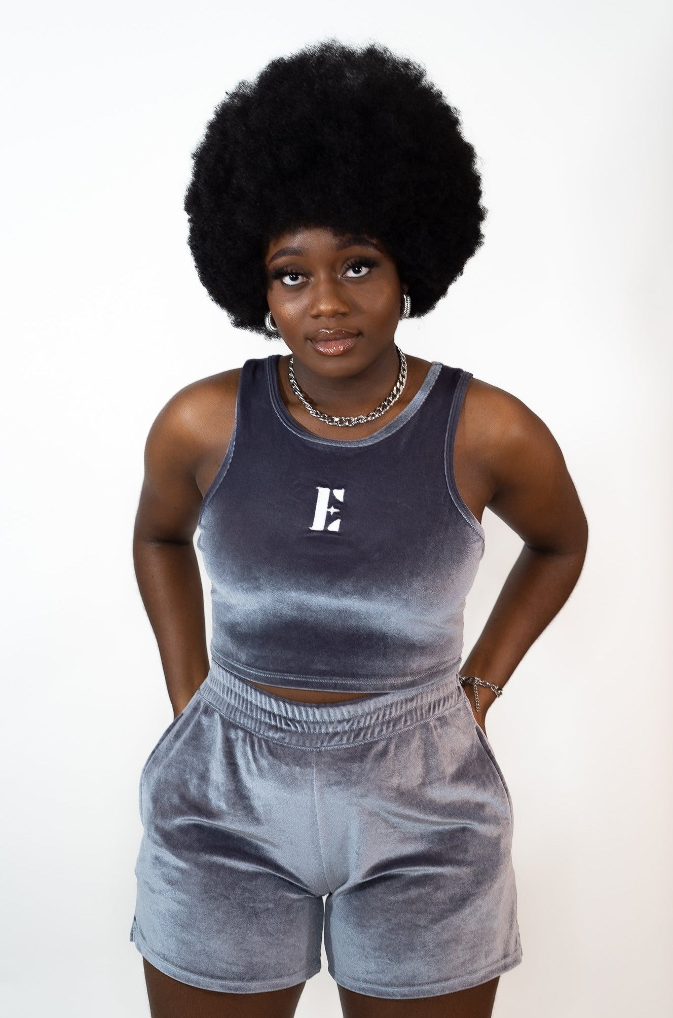 Model wearing grey velvet crop top and shorts. The crop top has the E's Element imprinted in white in the center. The model is also wearing an 18k silver stainless steel chain necklace and hoop earrings. Ella Icy Blue Velvet Set by E's Element.